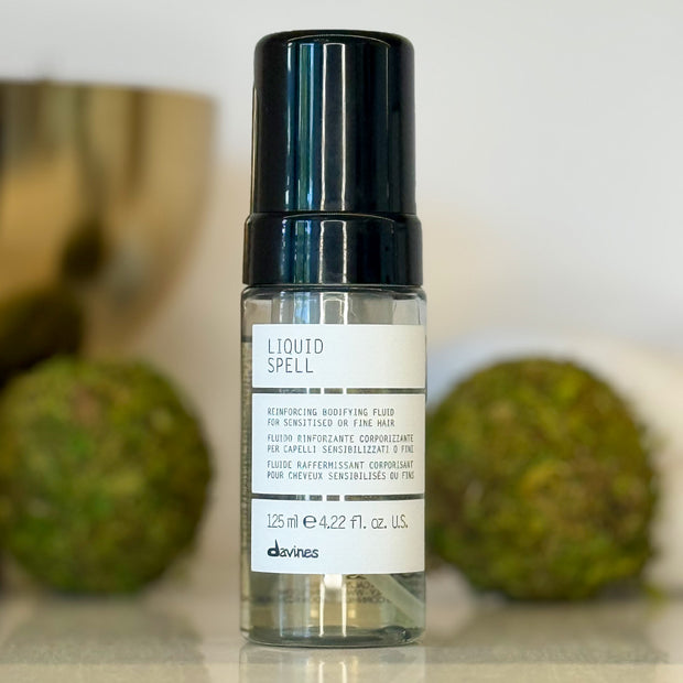 Bottle of 'Liquid Spell' hair product with a blurred background